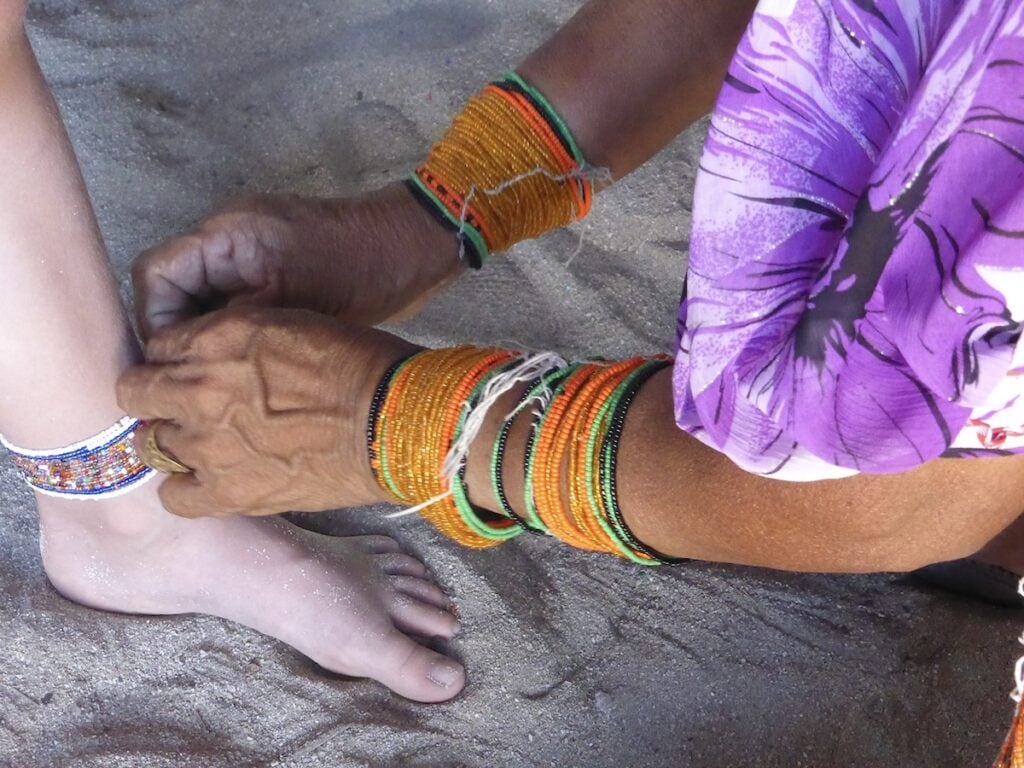 A Guna woman with beautiful beaded bracelets making an ankle bracelet for a visitor.